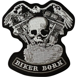 May include: A black embroidered patch featuring a central white skull positioned between two mechanical engine cylinders. Above the engine, two white eagles are depicted with wings spread. At the bottom, a banner displays the text BIKER BORN.