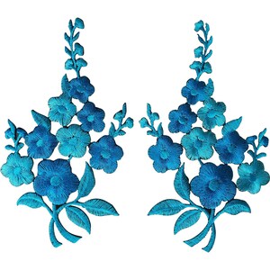 Op de afbeelding: Twee symmetrische geborduurde patches met levendige blauwgroene bloemen met vijf bloemblaadjes, stengels en bladeren. Het ingewikkelde draadwerk creëert een gestructureerd bloemmotief met verschillende blauwtinten, gerangschikt in een verticaal takpatroon.