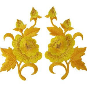 May include: A pair of symmetrical embroidered patches featuring vibrant yellow flowers with detailed petals, pointed leaves, and small closed buds. The design is rendered in a bright golden-yellow thread with intricate stitching patterns throughout.