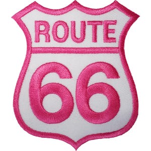 Könnte beinhalten: Ein schildförmiger, bestickter Aufnäher mit weißem Hintergrund und einem leuchtend pinkfarbenen Rand. Der Schriftzug ROUTE ist oben in Pink gestickt, und die Zahl 66 ist in großen pinkfarbenen Ziffern in der Mitte des Aufnähers zu sehen.