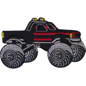 May include: An embroidered patch shaped like a monster truck. The vehicle is primarily black with red horizontal stripes along the side, yellow accents on the roof and front, and large, detailed grey tyres with black tread patterns and silver rims.