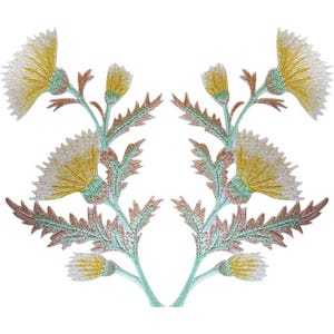 May include: Two symmetrical embroidered patches featuring yellow thistle flowers with light green stems and serrated leaves. The floral design includes detailed stitching in shades of yellow, pale green, and soft brown, creating a mirrored botanical motif.