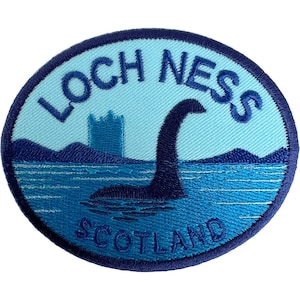 May include: An oval embroidered patch featuring a light blue sky and dark blue water. The text LOCH NESS is arched at the top, and SCOTLAND is at the bottom. A dark blue silhouette of the Loch Ness monster and a castle ruin are in the centre.