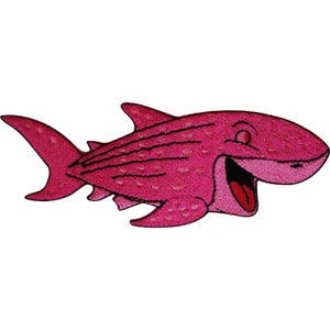 Puede incluir: Un parche bordado con forma de tiburón, que presenta un color rosa vibrante con manchas de color rosa más oscuro, contornos cosidos en negro y una boca muy abierta que revela una lengua roja, diseñado con una estética de dibujos animados y acabado texturizado.