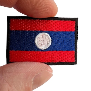 May include: A rectangular embroidered patch featuring the flag of Laos, consisting of a wide blue horizontal band in the center flanked by two red horizontal bands, with a white circular emblem centered on the blue stripe and a black border.