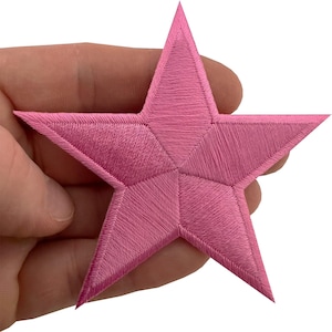 May include: A five-pointed star patch featuring dense, vibrant pink embroidery thread. The design showcases a geometric pattern with distinct stitched sections radiating from the centre to each point, creating a textured, raised surface finish.