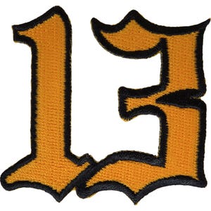 Könnte beinhalten: Ein gestickter Aufnäher mit der Zahl 13 in einer kräftigen, gotischen Schriftart. Die Ziffer ist in einem leuchtenden Goldgelb gehalten und mit einem dicken, tiefschwarzen Rand versehen, der die Form umreißt und ein kontrastreiches Design bildet.