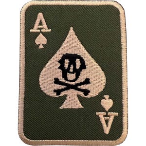 Könnte beinhalten: Ein rechteckiger bestickter Aufnäher mit olivgrünem Hintergrund und hellbeigem Rand. Das Design zeigt ein großes hellbeiges Pik-Symbol mit einem schwarzen Totenkopf und gekreuzten Knochen sowie den Buchstaben A und ein kleines Pik in den Ecken.