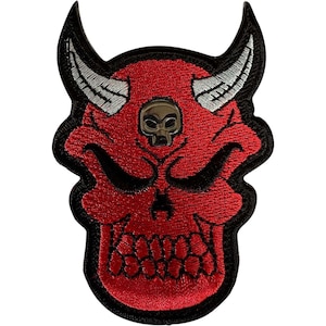 Puede incluir: Un parche bordado que muestra una calavera de diablo roja con cuernos plateados prominentes y un pequeño emblema de calavera metálica centrado en la frente. El diseño está delineado con hilo negro grueso, creando un contraste con el rojo.