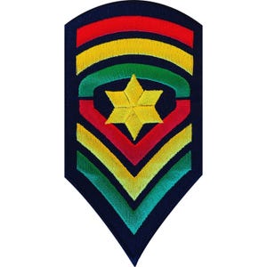 May include: A shield-shaped embroidered patch on a dark blue background featuring a central yellow six-pointed star. The design includes three horizontal arched stripes in red, yellow, and green, followed by three downward-pointing chevrons in red, yellow, and green.