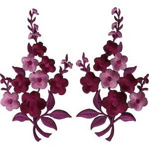 Puede incluir: Dos parches bordados florales simétricos que presentan racimos de flores de cinco pétalos y hojas en varios tonos de burdeos intenso, magenta y rosa claro. Los diseños están orientados verticalmente con tallos en la base y capullos arriba.