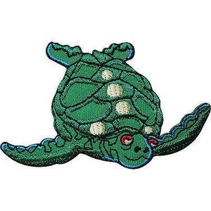 Puede incluir: Un parche bordado con forma de tortuga marina. La tortuga presenta un cuerpo de color verde vibrante con un caparazón verde oscuro, acentuado por manchas circulares de color crema en el caparazón y un borde azul que perfila las aletas y la cabeza.