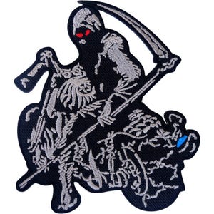 May include: An embroidered patch featuring a grim reaper figure in black and silver thread. The figure has glowing red eyes, wears a hooded cloak, and holds a large scythe. The design includes intricate skeletal details and a small blue accent.