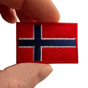 Può includere: Una toppa ricamata rettangolare che raffigura la bandiera della Norvegia. Il design presenta uno sfondo rosso brillante con una croce orizzontale e verticale blu scuro, delineata da sottili cuciture bianche. I bordi della toppa sono rifiniti in rosso.