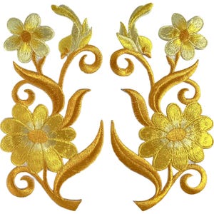 Può includere: Una coppia di toppe ricamate simmetriche raffiguranti fiori giallo oro con steli e foglie a spirale. Ogni toppa presenta un grande fiore inferiore e un fiore più piccolo superiore, realizzati con filo giallo brillante e cuciture dettagliate.
