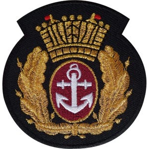 Op de afbeelding: Een ronde zwarte geborduurde patch met een centraal bordeauxrood ovaal met een wit anker. Het ontwerp is omringd door gouden geborduurde laurierbladeren en bekroond met een gouden kroon met kleine rode accenten op de bovenste punten.
