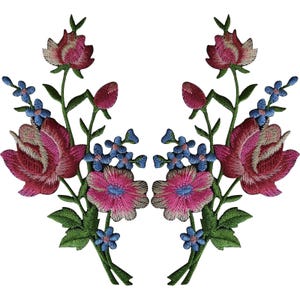May include: Two symmetrical embroidered floral patches featuring large dark pink roses, smaller bright pink blossoms, and tiny light blue flowers with green stems and leaves. The intricate needlework creates a detailed botanical design.