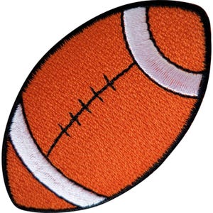 May include: An embroidered patch shaped like an American football. The patch features a textured orange surface with white stripes at both ends and black stitched detailing representing the laces running down the centre of the ball.