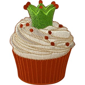 Könnte beinhalten: Ein gestickter Aufnäher in Form eines Cupcakes mit rostfarbener Basis, weißem Zuckerguss und kleinen roten Streuseln. Eine leuchtend grüne Krone mit drei Zacken sitzt auf dem Zuckerguss und hat kleine rote Akzente an den Spitzen der Krone.