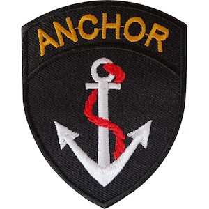 Pode incluir: Um emblema bordado em forma de escudo com fundo preto. A palavra ANCHOR está bordada em fio dourado no topo. Uma âncora branca está centrada no meio, envolvida por uma corda vermelha que se enrola em torno da haste vertical.