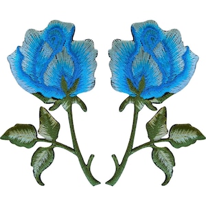 May include: Two embroidered patches featuring a blue rose design. Each patch displays a vibrant blue flower head with white highlights, a green stem, and two green leaves. The embroidery uses varied shades of blue and green thread to create texture and depth on the petals and foliage against a plain white background.