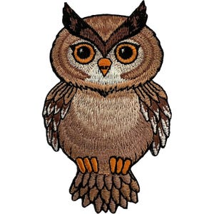 May include: An embroidered owl patch featuring shades of brown, tan, and white thread. The owl has large, round orange eyes, a small orange beak, and detailed feather stitching throughout its body, wings, and tail, finished with a black border.