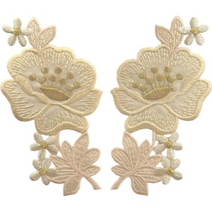 May include: Two symmetrical embroidered floral patches featuring large cream-coloured peony-like blossoms with gold-toned centres, accented by smaller five-petaled flowers and detailed leaves in soft beige and pale pink thread on a fabric base.