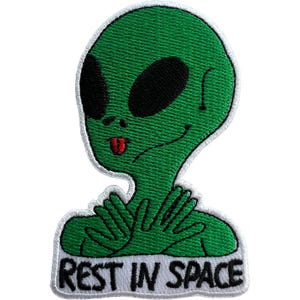 May include: An embroidered patch featuring a green alien with large black eyes, a small red tongue, and hands crossed over its chest. Below the alien, the text REST IN SPACE is stitched in black capital letters on a white background border.