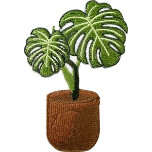 Puede incluir: Un parche bordado que muestra una planta monstera en maceta. La planta tiene dos hojas verdes grandes y divididas con detalles de nervaduras blancas. La maceta es de color marrón sólido con un patrón de puntadas texturizado y borde blanco.