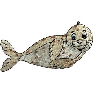 May include: An embroidered iron-on patch featuring a cartoon seal with light tan fur and brown spots. The seal has a smiling face, large dark eyes, whiskers, and a flipper-like tail. The design is rendered in detailed thread work.