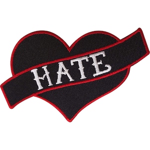 May include: A black heart-shaped embroidered patch with a red border. A black banner crosses the heart diagonally, featuring the word HATE stitched in white capital letters. The design has a textured fabric appearance with visible thread stitching.