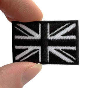 May include: A rectangular embroidered patch featuring a black and white Union Jack flag design. The patch has a thick black border and a detailed stitched pattern representing the flag's cross and diagonal lines in a high-contrast monochrome colour scheme.