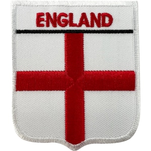 May include: A shield-shaped embroidered patch featuring the flag of England with a white background and a red cross. The word ENGLAND is stitched in red capital letters across the top section, separated from the cross by a thin black horizontal line.