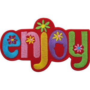 May include: An embroidered patch featuring the word enjoy in colourful letters against a red background. The letters are blue, pink, yellow, purple, and green, each decorated with small, multi-coloured flower motifs throughout the design.