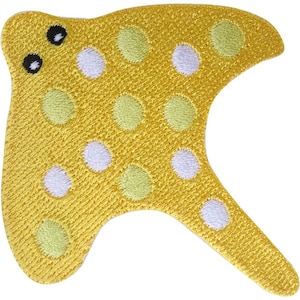 May include: A yellow embroidered patch shaped like a stingray with two black eyes. The surface features a repeating pattern of light green and white circular polka dots stitched into the fabric, covering the body and the extended tail section.