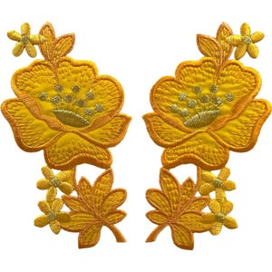 May include: Two matching embroidered patches featuring a large yellow flower with golden centre details, accompanied by smaller yellow blossoms and pointed leaves. The design is rendered in vibrant yellow thread with metallic gold accents throughout.
