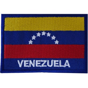 Puede incluir: Un parche bordado rectangular que presenta la bandera de Venezuela con franjas horizontales amarilla, azul y roja. Un arco de ocho estrellas blancas está centrado en la franja azul, y la palabra VENEZUELA está bordada en letras mayúsculas blancas.