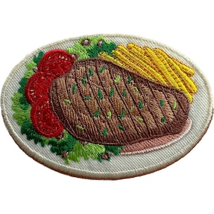 May include: An oval embroidered patch featuring a brown grilled steak with visible char marks, a side of yellow french fries, three bright red tomato slices, and green lettuce leaves, all set against a white background with a stitched border.