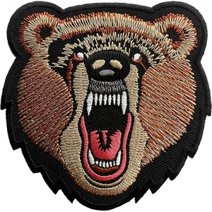 May include: An embroidered patch featuring the head of a snarling bear with its mouth open, revealing white teeth and a pink tongue. The bear is rendered in shades of brown, tan, and black thread against a solid black background border.