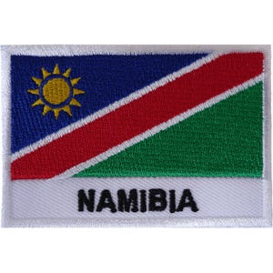 May include: A rectangular embroidered patch featuring the flag of Namibia. The design includes a blue field with a yellow sun, a diagonal red stripe bordered by white, and a green field. The word NAMIBIA is embroidered in black on a white base.