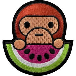 May include: An embroidered patch featuring a cartoon monkey with brown fur and a tan face peeking over a slice of watermelon. The watermelon slice has a bright pink center with black seeds, a white rind, and a light green outer edge, all outlined in black.