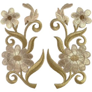 May include: Two symmetrical gold-toned embroidered floral patches featuring detailed stitching of daisy-like flowers, swirling vine stems, and pointed leaves. The metallic thread creates a shimmering texture across the botanical motifs.