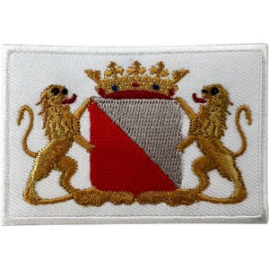 Peut inclure: Un écusson brodé rectangulaire sur fond blanc représentant un blason central divisé en diagonale en sections rouge et argent. Le blason est surmonté d'une couronne dorée et flanqué de deux lions dorés aux langues et queues rouges.