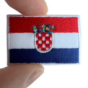 Puede incluir: Un parche bordado rectangular que presenta la bandera nacional de Croacia. El diseño consta de franjas horizontales roja, blanca y azul con el escudo de armas croata centrado, mostrando un escudo ajedrezado rojo y blanco y una corona.