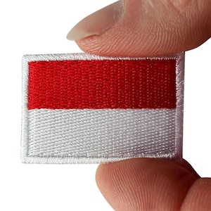 May include: A rectangular embroidered patch featuring the national flag of Indonesia, consisting of two horizontal bands of equal height with a vibrant red colour on the top half and a clean white colour on the bottom half, finished with a white border.