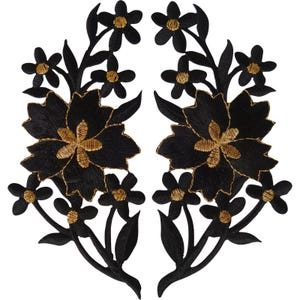 May include: A pair of symmetrical embroidered patches featuring black floral designs with gold-coloured centres. Each patch displays a large central flower surrounded by smaller blossoms, stems, and leaves, all rendered in detailed black thread.