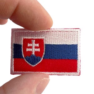 Pode incluir: Um emblema retangular bordado com a bandeira nacional da Eslováquia. O design consiste em três faixas horizontais nas cores branca, azul e vermelha, com o brasão eslovaco centralizado à esquerda, exibindo uma cruz dupla branca.