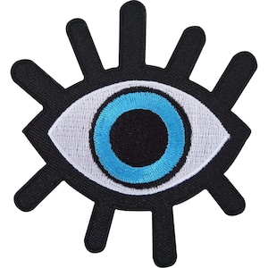 May include: An embroidered patch in the shape of an eye with a black outline and radiating black lashes. The eye features a white sclera, a bright blue iris, and a solid black pupil, all rendered in dense thread stitching on a black background.