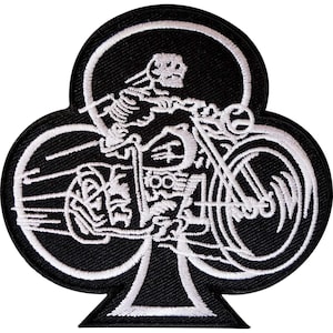 May include: A black and white embroidered patch in the shape of a club playing card suit. The design features a skeleton riding a motorcycle, with white thread detailing the skeleton, the bike, and motion lines against a solid black background.