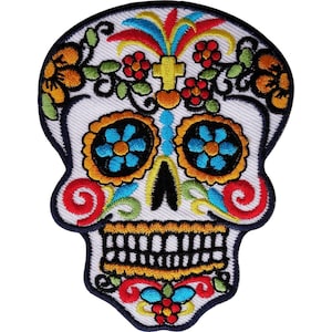 May include: An embroidered patch shaped like a skull with a white base and colorful details. The design features blue flower eye sockets, a yellow jaw, and floral accents in red, orange, green, and blue. A yellow cross sits on the forehead.